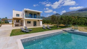 Uma casa moderna de dois andares com piscina, área de estar externa e montanhas ao fundo.