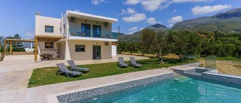 A modern two-story house with a swimming pool, outdoor seating, and a mountainous backdrop.