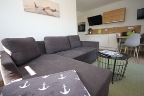 A modern living room with a grey sofa, a small round table, and a kitchen area in the background. - FW Pont Port, Germany (Wustrow)