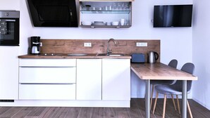A modern kitchen with a built-in oven, a coffee maker, a sink, and a dining area with a table and chairs. - FW Port Bridge, Germany (Wustrow)
