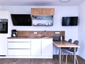 Et moderne køkken med indbygget ovn, kaffemaskine, vask og et spiseområde med bord og stole.