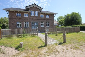 En toetages murbygning med en hovedindgang, et træhegn og en græsplæne foran.