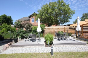 A patio with outdoor furniture, a small garden, and a brick house in the background. - FW Backbord Peildeck (Wustrow)