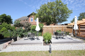 A patio with outdoor furniture, a small garden, and a brick house in the background.