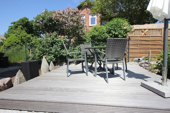 A wooden deck with outdoor furniture, a bamboo fence, and a house in the background.