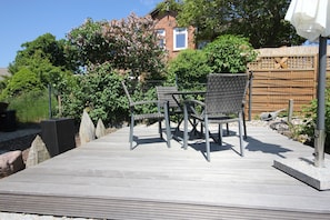 A wooden deck with outdoor furniture, a bamboo fence, and a house in the background.