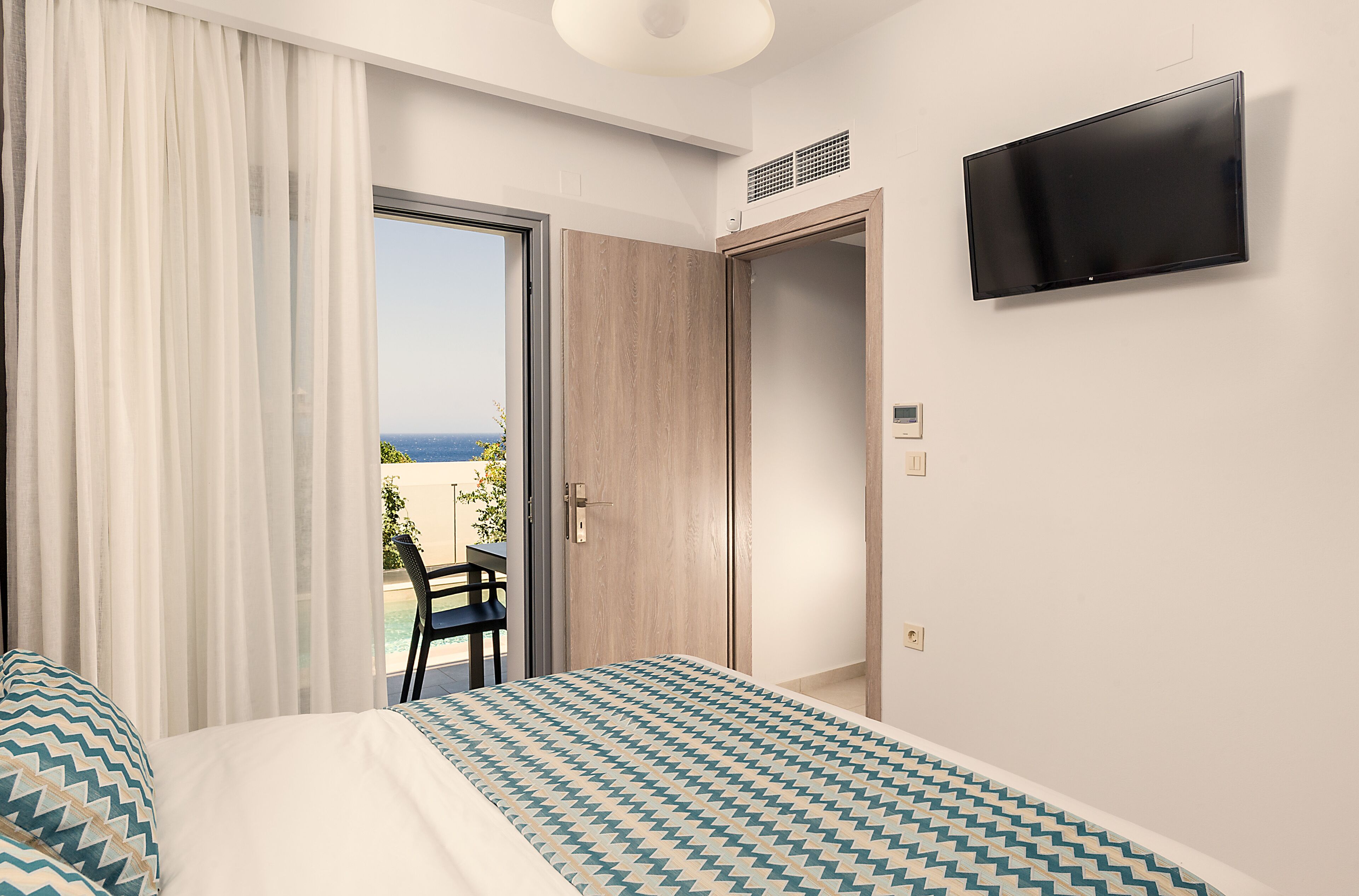 A hotel room with a bed, a TV, a door leading to a balcony, and a chair.