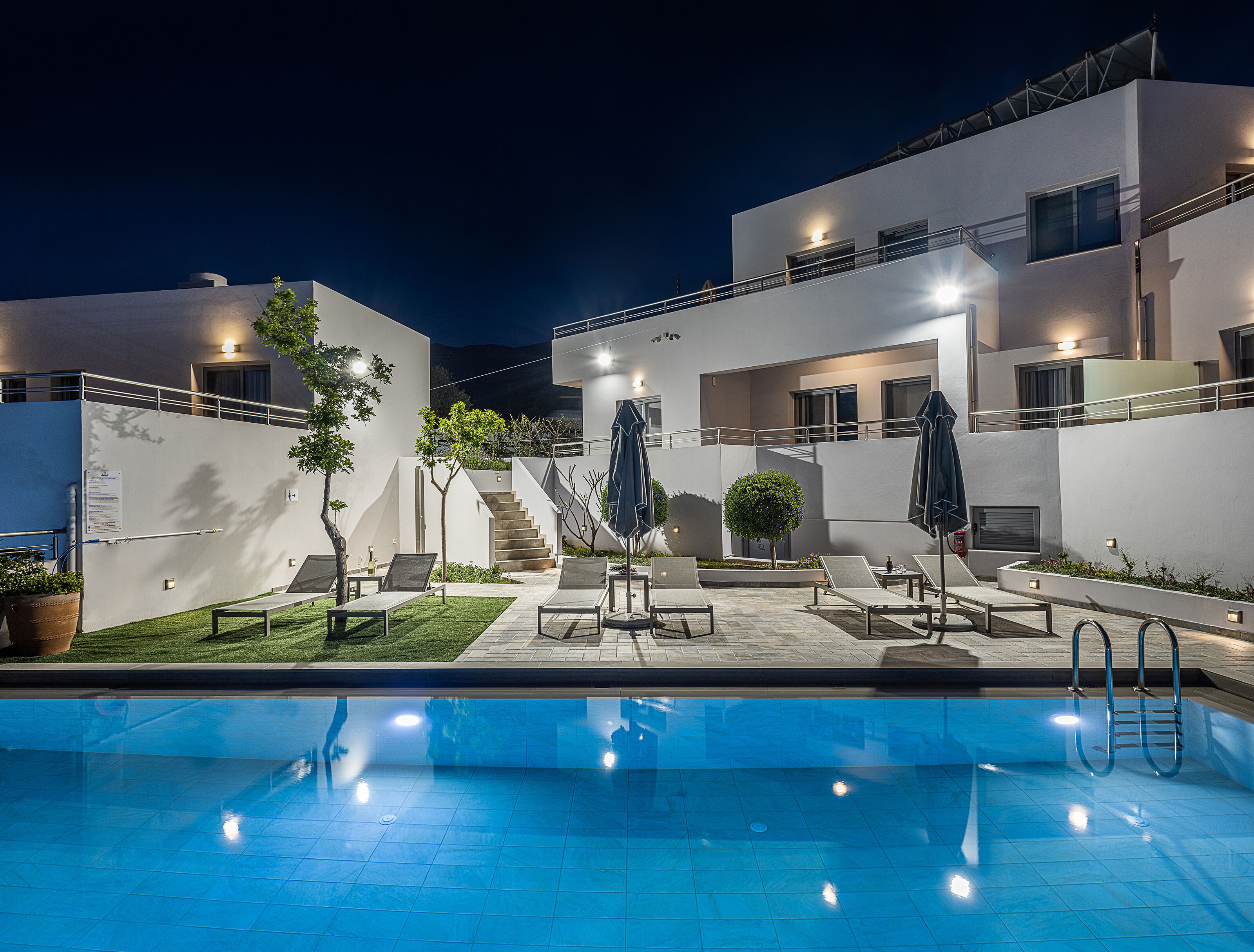 A modern outdoor pool area with lounge chairs, umbrellas, and a staircase leading to a building.