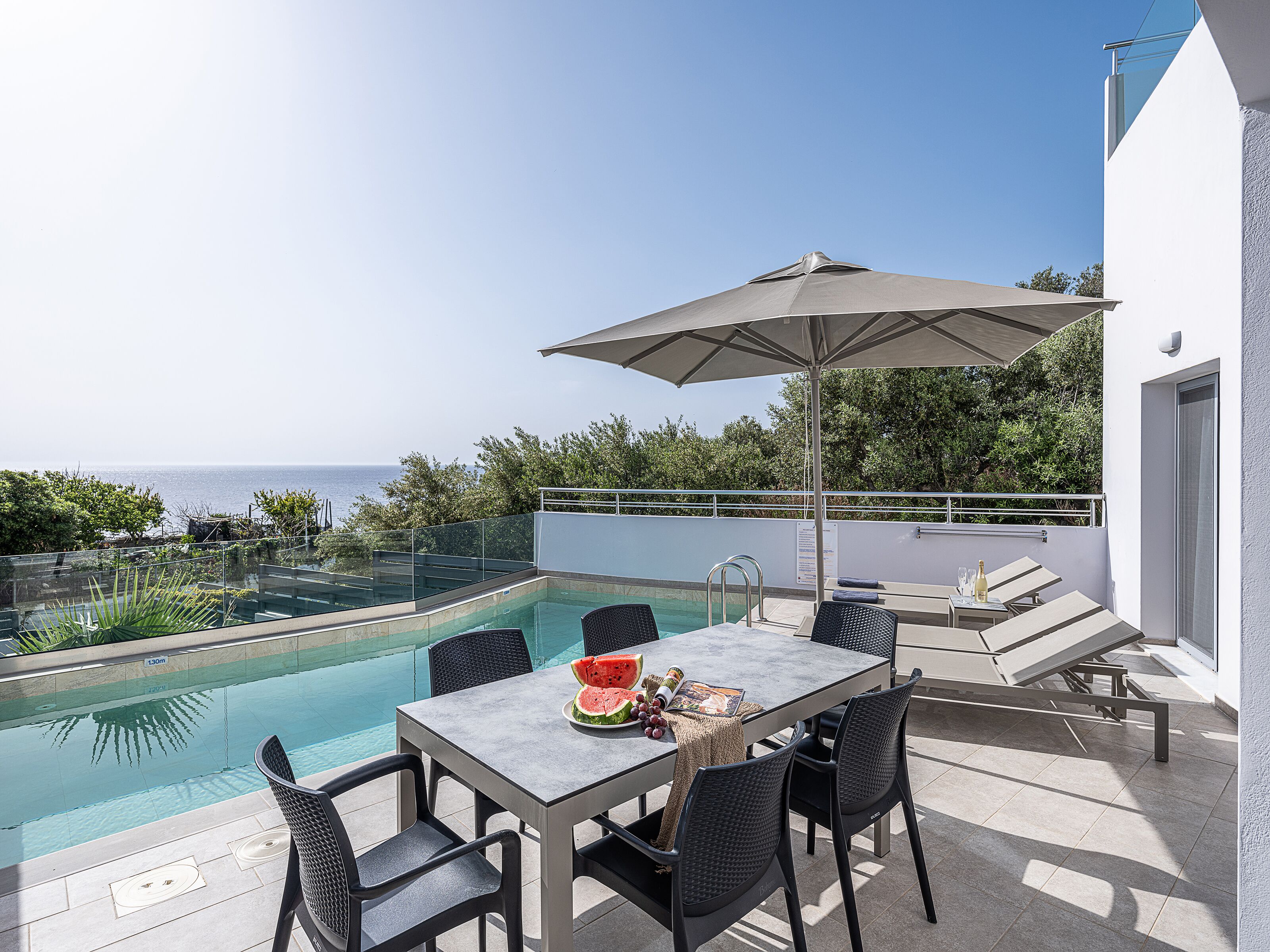 Zona junto a la piscina con una mesa, sillas y una sombrilla.