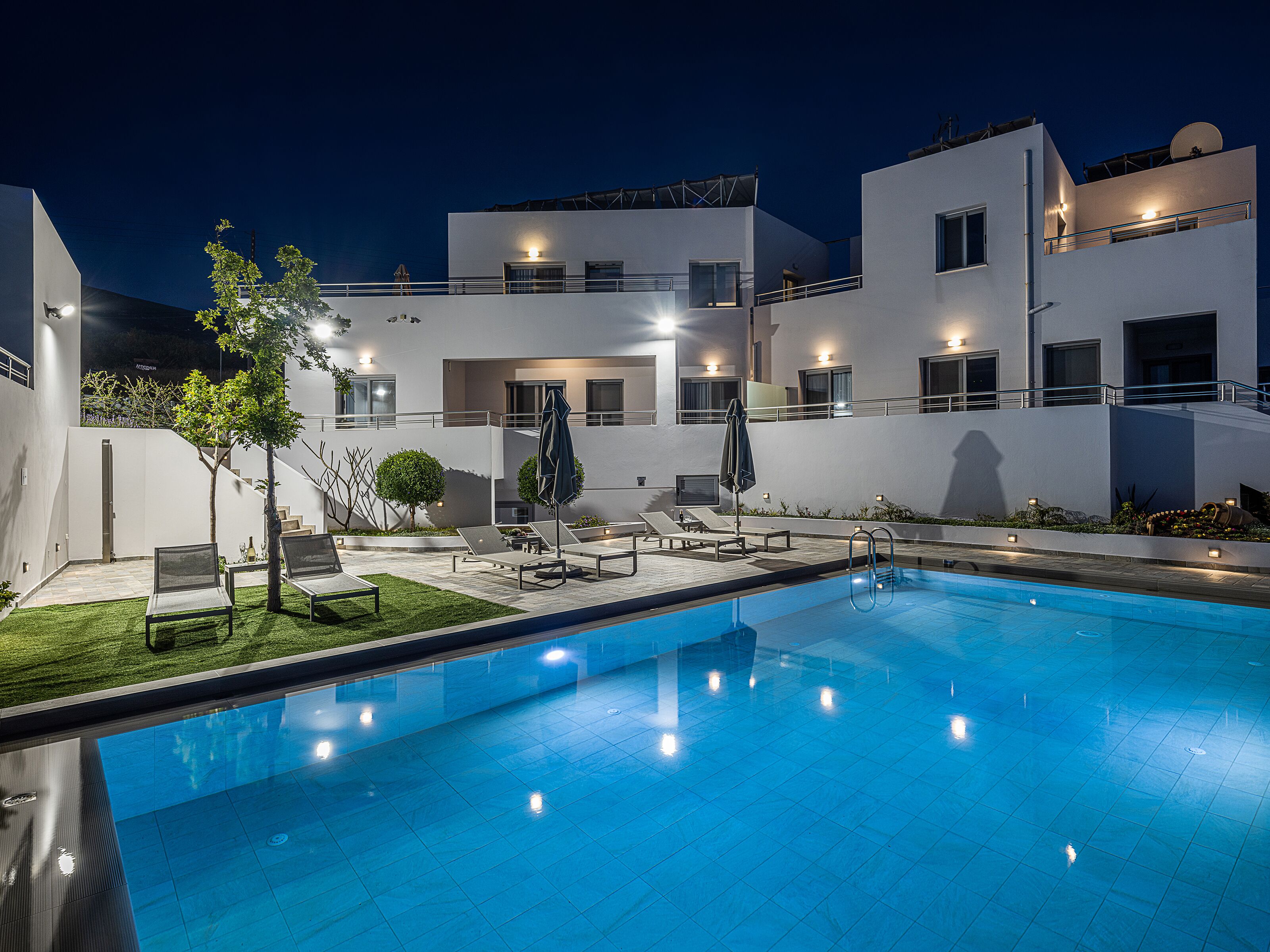 A modern pool area with a clear blue pool, sun loungers, and a well-lit outdoor space.