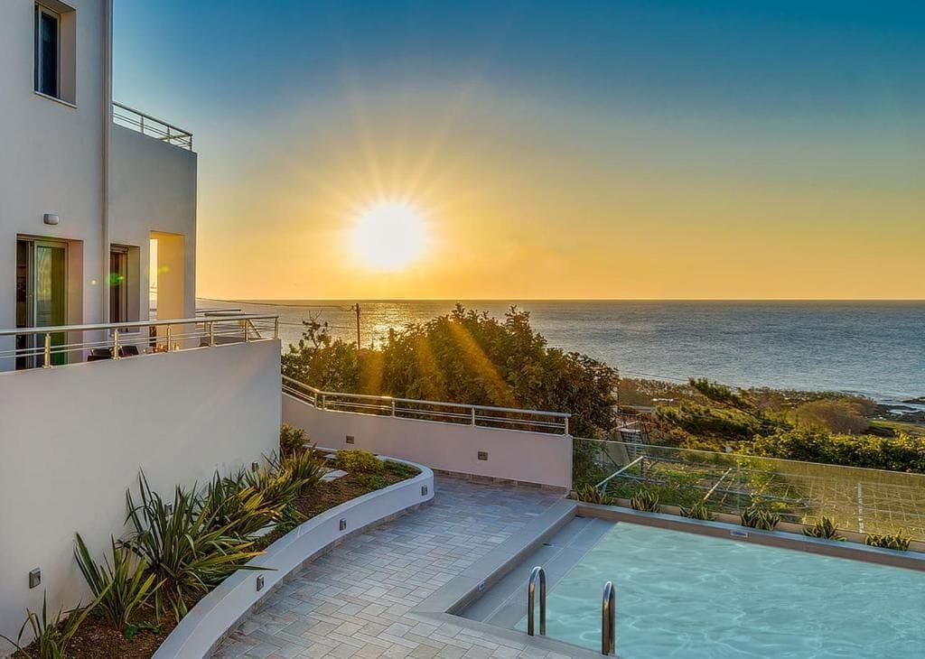 A modern building with a pool overlooking the ocean at sunset.