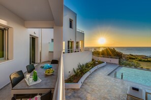 Een modern balkon met een zwembad, eethoek en uitzicht op de ondergaande zon boven de zee.