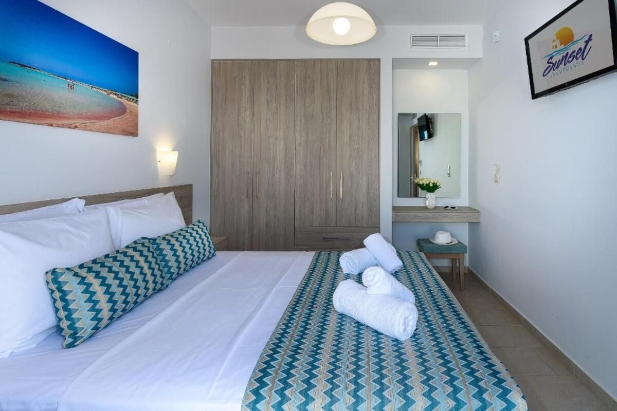 A hotel room with a bed, a wardrobe, a vanity with a mirror, and a framed picture on the wall.