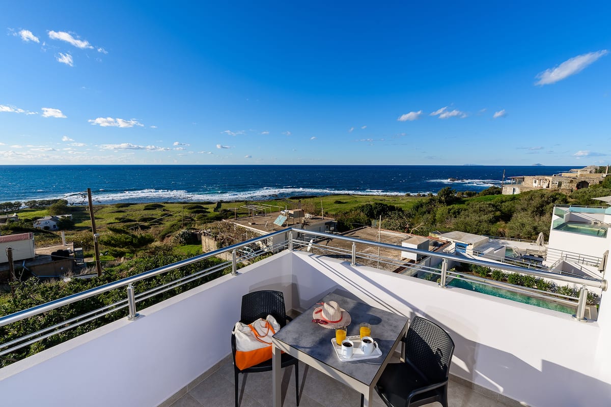 Een balkon met een tafel, stoelen en uitzicht op zee.