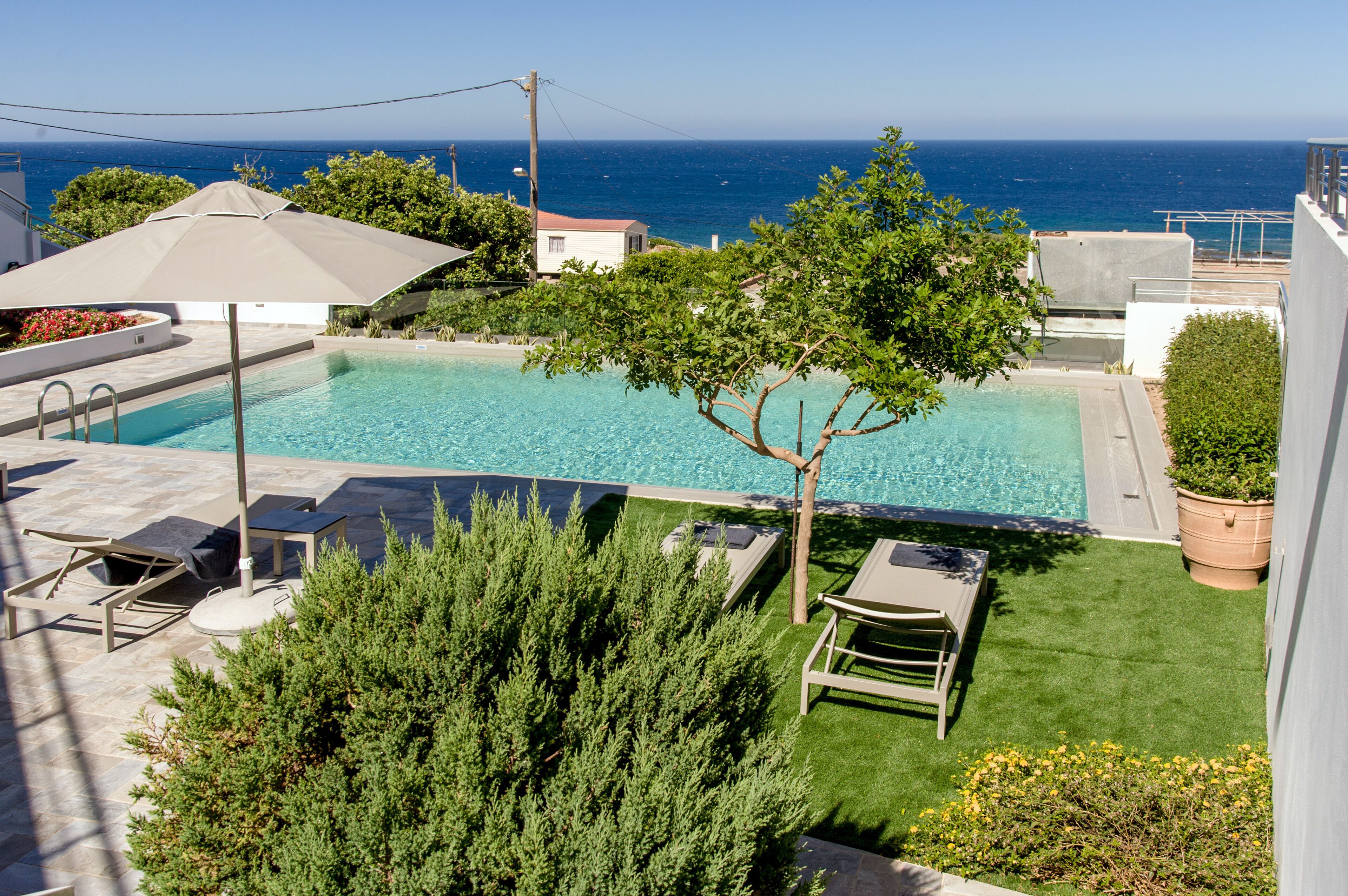 Une piscine avec vue sur l’océan, entourée de verdure et agrémentée de mobilier d’extérieur.