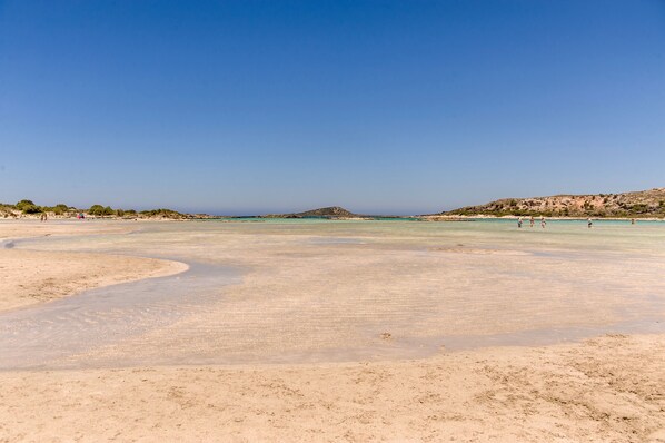 A wide sandy beach with clear blue water and a distant hill. - Sunset Elafonisi Apartments (Kissamos)