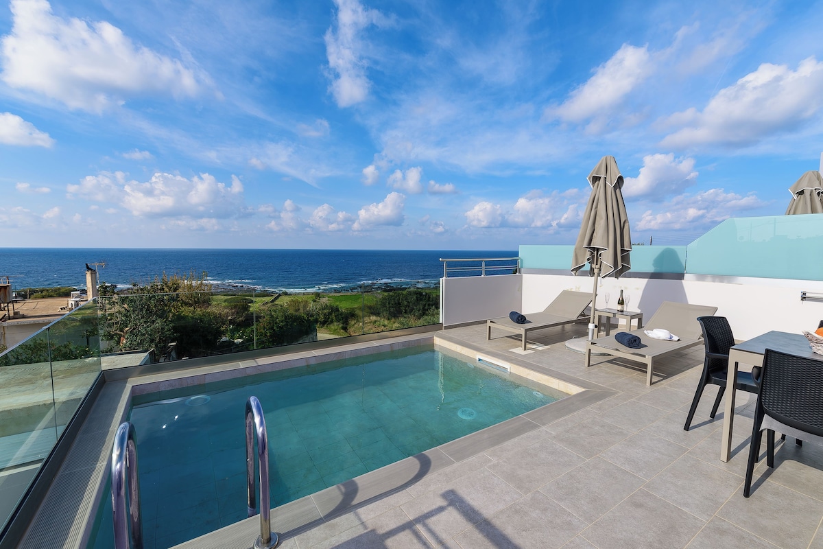 A rooftop pool with a clear view of the ocean, a table with chairs, and a bar area.