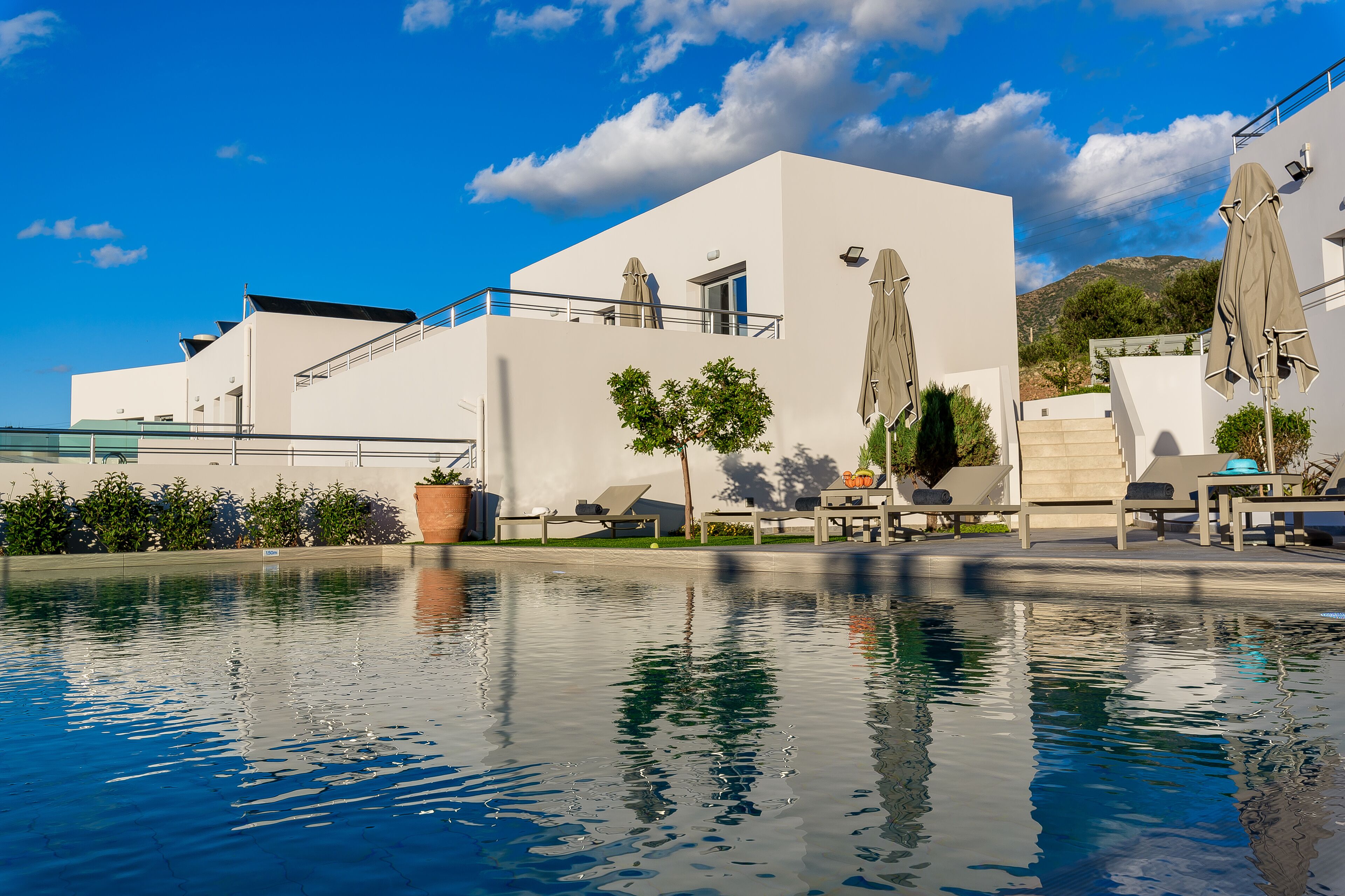A modern building with a pool, outdoor seating, and umbrellas.