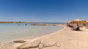 Una playa con agua cristalina, rocas y sombrillas de paja.