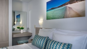 Habitación de hotel con una cama, una mesita de noche, un espejo, un cuadro en la pared y un banco.