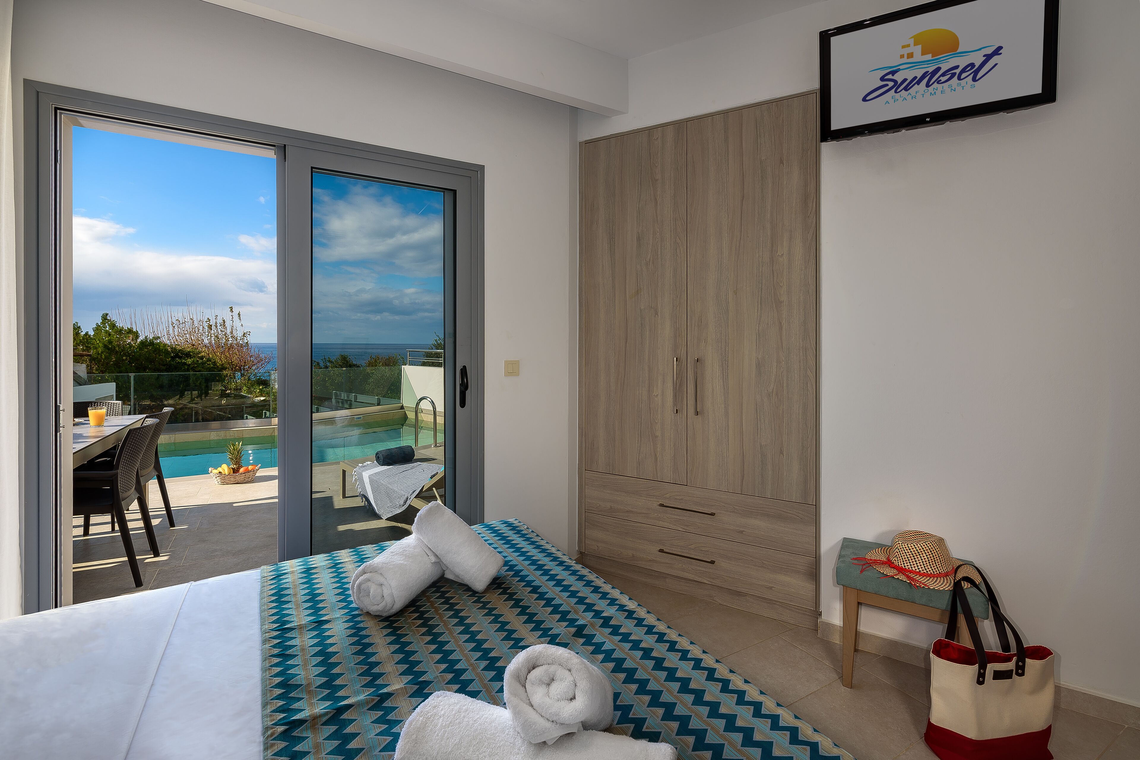 Habitación de hotel con cama, banco, armario grande y vista a una piscina y al océano.