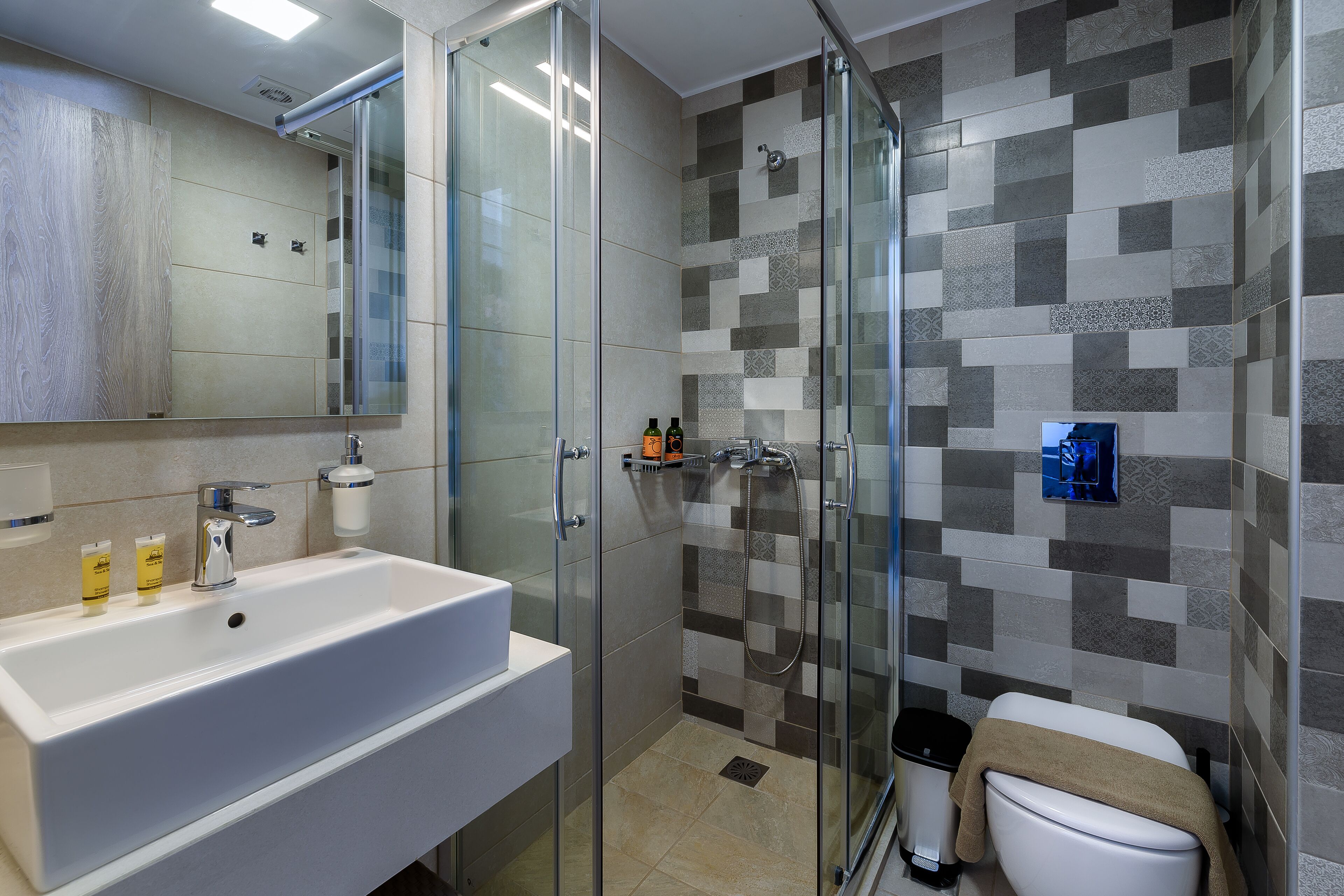 Een moderne badkamer met een groot wit wastafelmeubel, een glazen douchecabine en een betegelde douchewand.