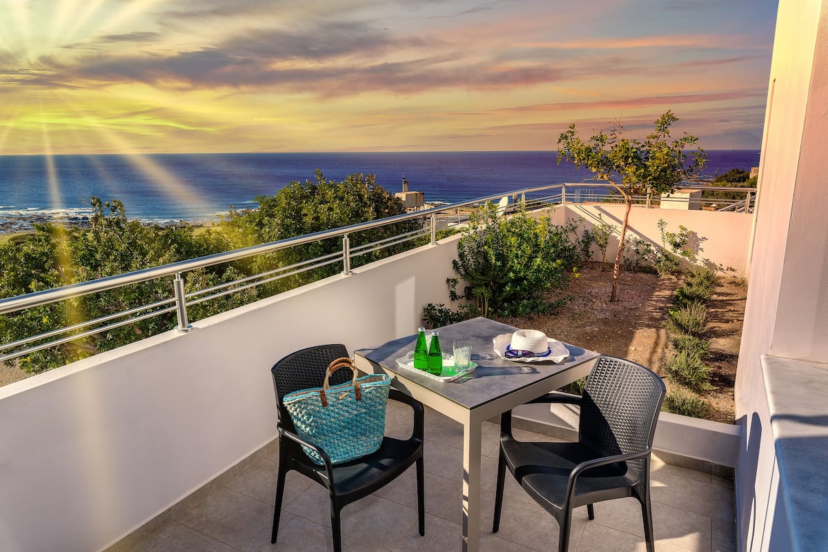 Een balkon met een tafel, stoelen en uitzicht op zee.
