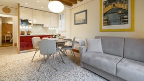 A modern living room with a grey sofa, a dining area with a table and chairs, a kitchen with white cabinets, and a large painting on the wall. - Rialto Sant'Aponal Prestige by Wonderful Italy (Venice)