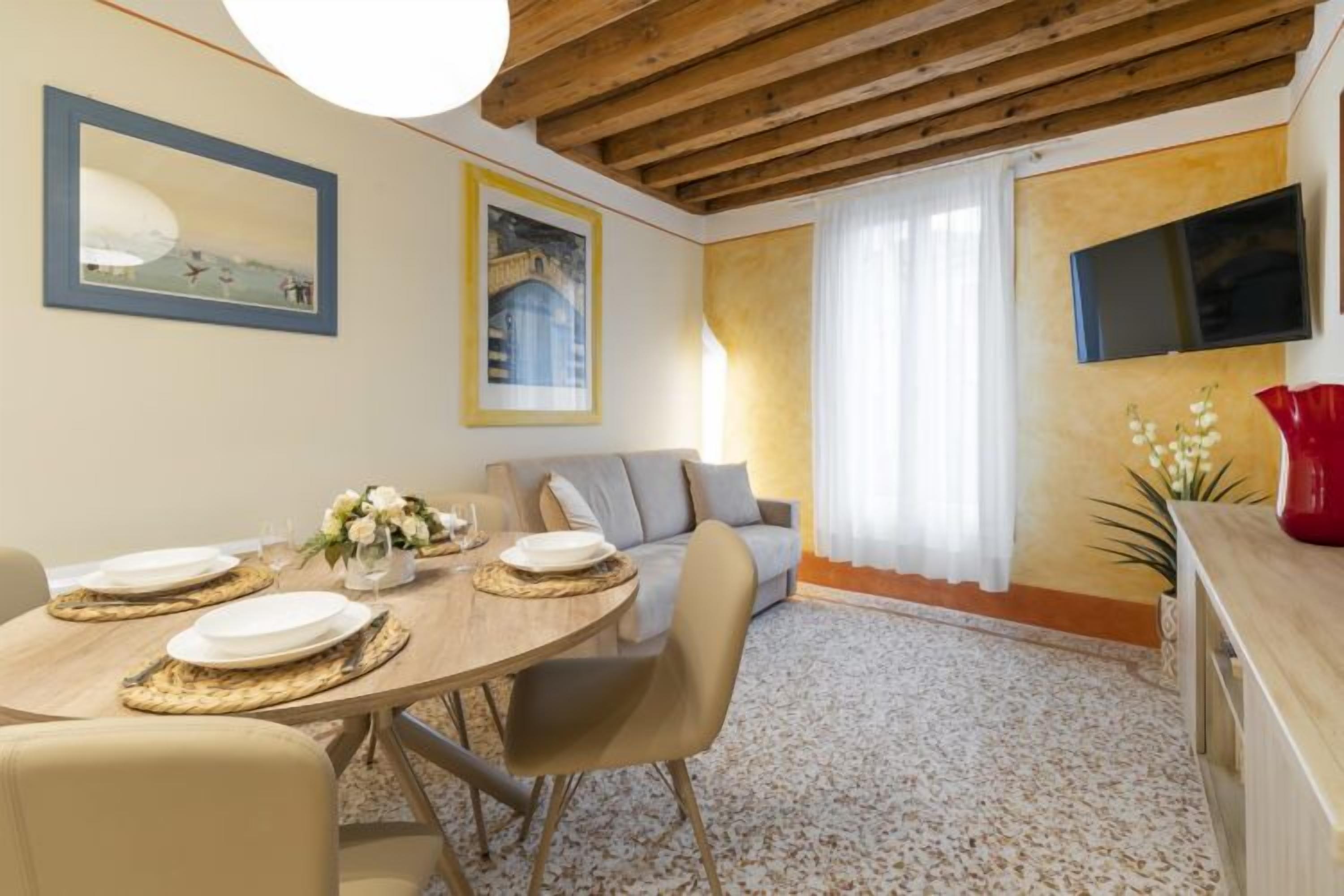 Un coin repas avec une table en bois dressée pour quatre personnes, un canapé et un téléviseur fixé au mur.
