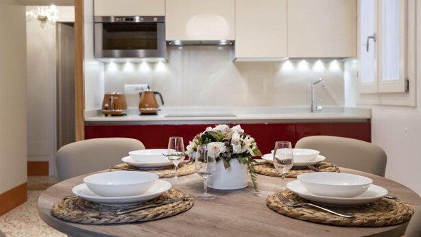 A modern kitchen with white cabinets, a stainless steel range hood, and a red countertop. - Rialto Sant'Aponal Prestige by Wonderful Italy (Venice)