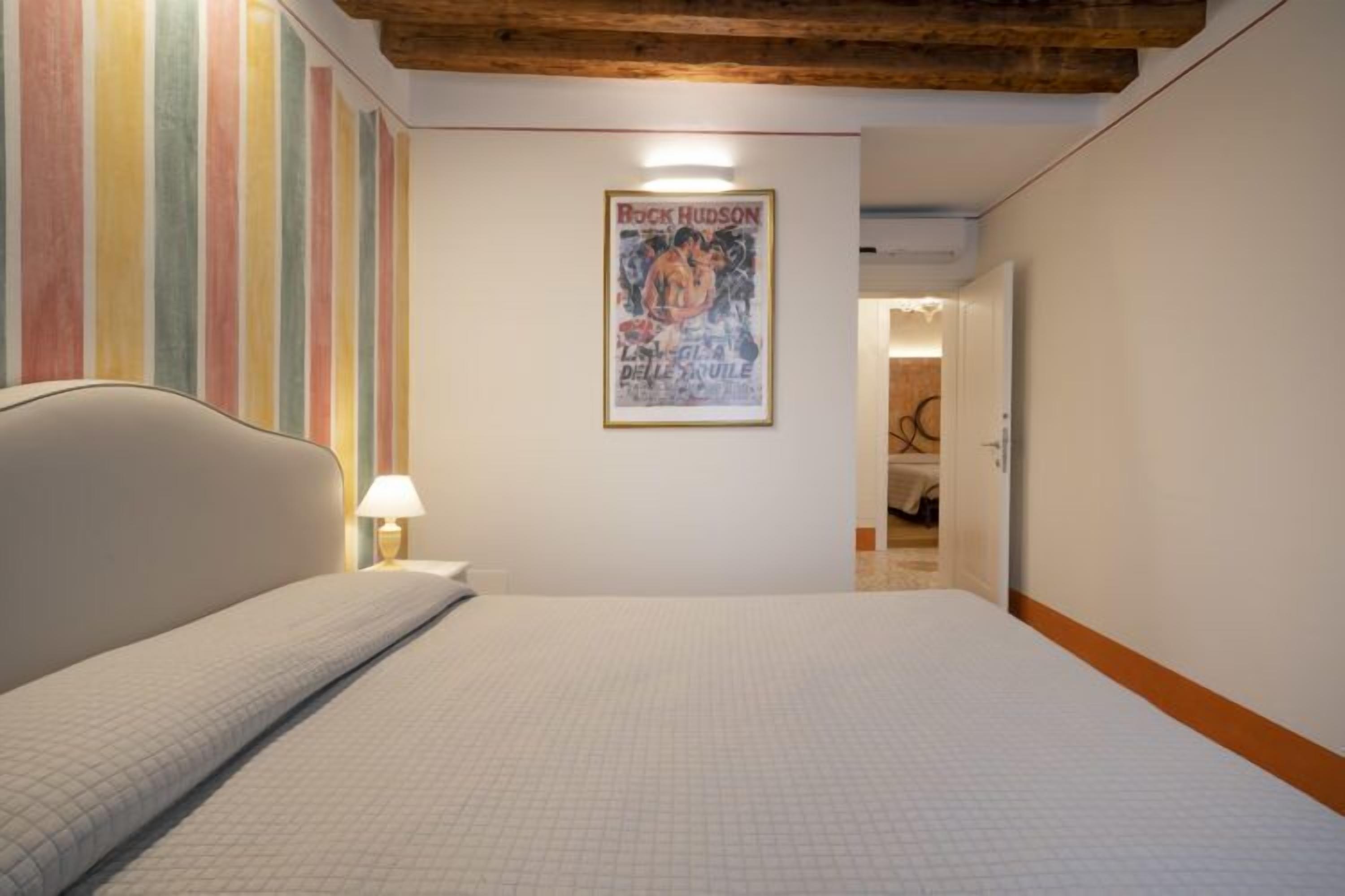 A bedroom with a bed, a lamp, a poster on the wall, and a wooden ceiling.
