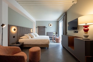 Una habitación de hotel moderna con cama, mesita de noche, lámpara, zona de estar y televisor.