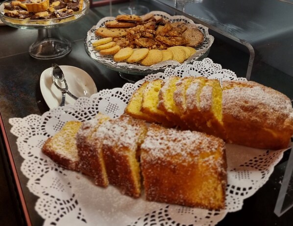 Una mesa con una variedad de productos horneados, incluyendo hogaza de pan y galletas, sobre una mesa de vidrio con un copo de encaje.