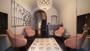 A reception area with a modern chandelier, a reception desk with 'VIS' illuminated, and two plush armchairs. - Vis Urban Suites & Spa (Bari)