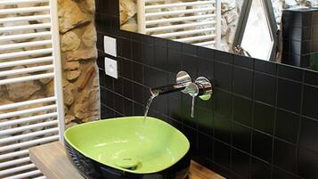 Un lavandino in ceramica verde con un rubinetto cromato, posto di fronte a una parete rivestita di piastrelle nere con un elemento decorativo in pietra.
