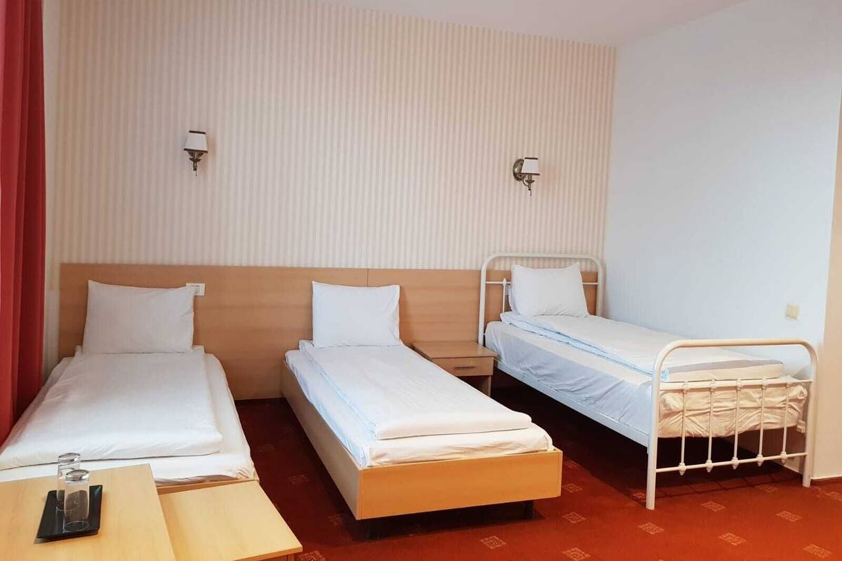 A hotel room with three single beds, a wooden nightstand, and a red curtain.