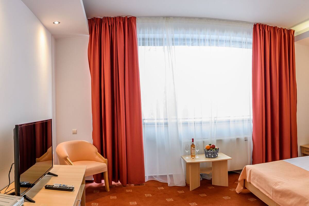 A hotel room with a bed, a desk with a lamp, a chair, and a TV.