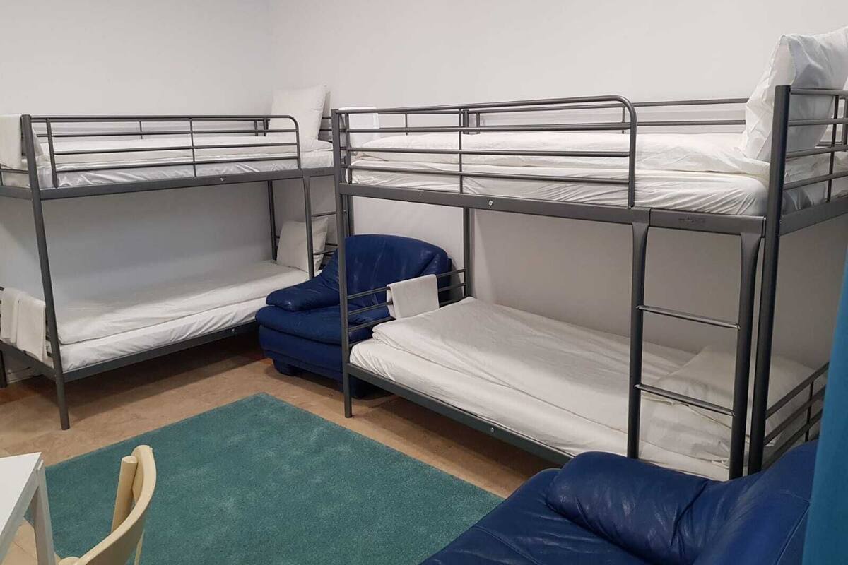A dormitory room with bunk beds, a green carpet, and a chair.