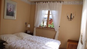 A bedroom with a large bed, a nightstand, a bedside lamp, a window with curtains, a wall-mounted light fixture, and a framed picture. - Holiday Home Gamla Vägen Konga (Tingsryd)