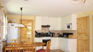 A compact kitchen with white cabinets, a microwave, and a stove. There is a dining table with chairs and a hanging light fixture. - Holiday Home Gamla Vägen Konga (Tingsryd)