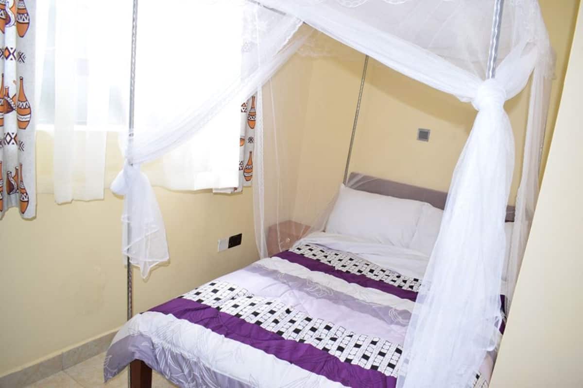 A single bed with a canopy, a patterned bedspread, and curtains with a cultural design.
