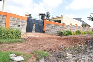 A gated entrance with a brick wall and orange accents, leading to a building with a sloped roof.