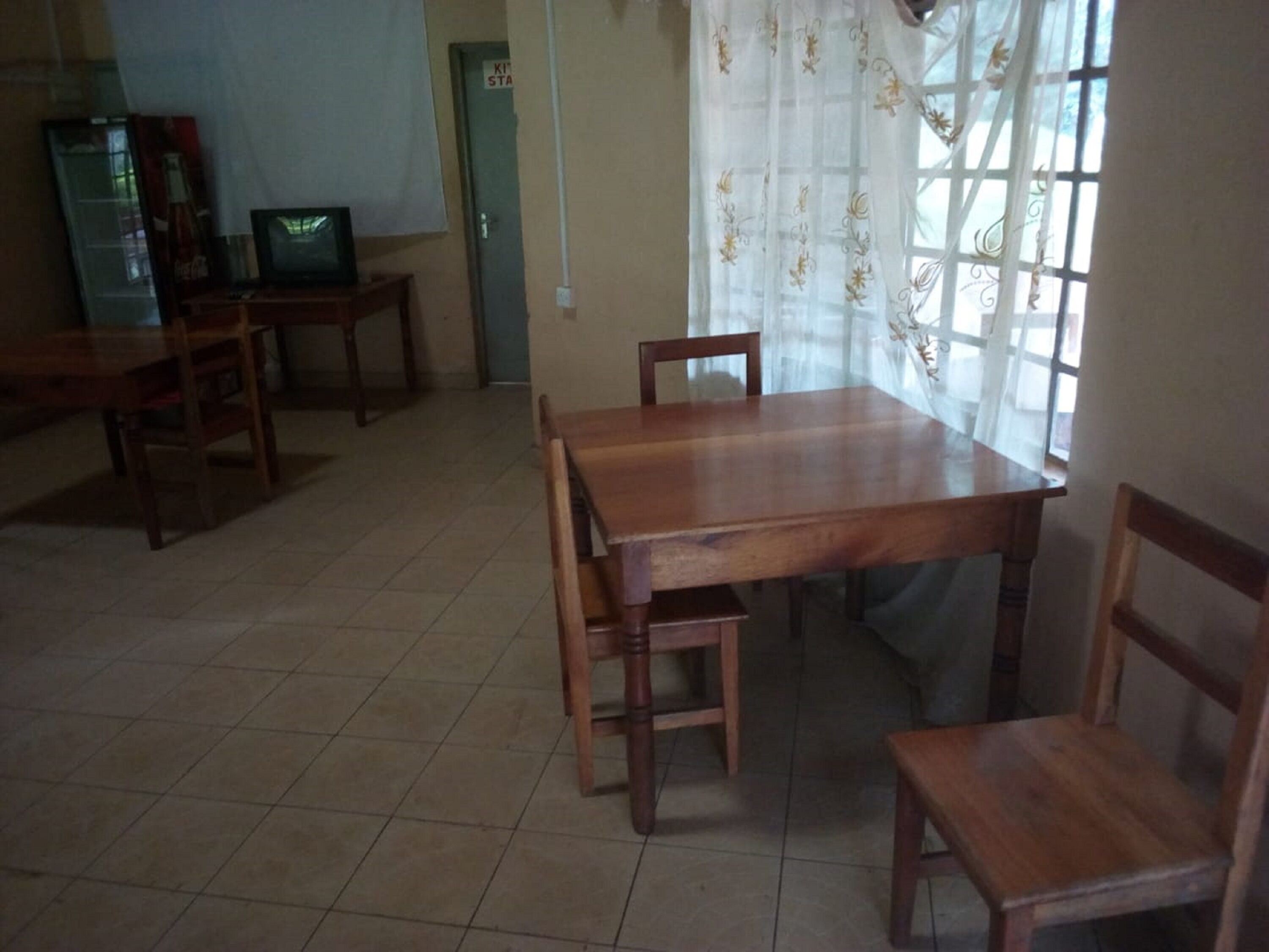 Uma área de refeições com uma mesa e cadeiras de madeira, uma televisão em um suporte e uma porta com uma placa.