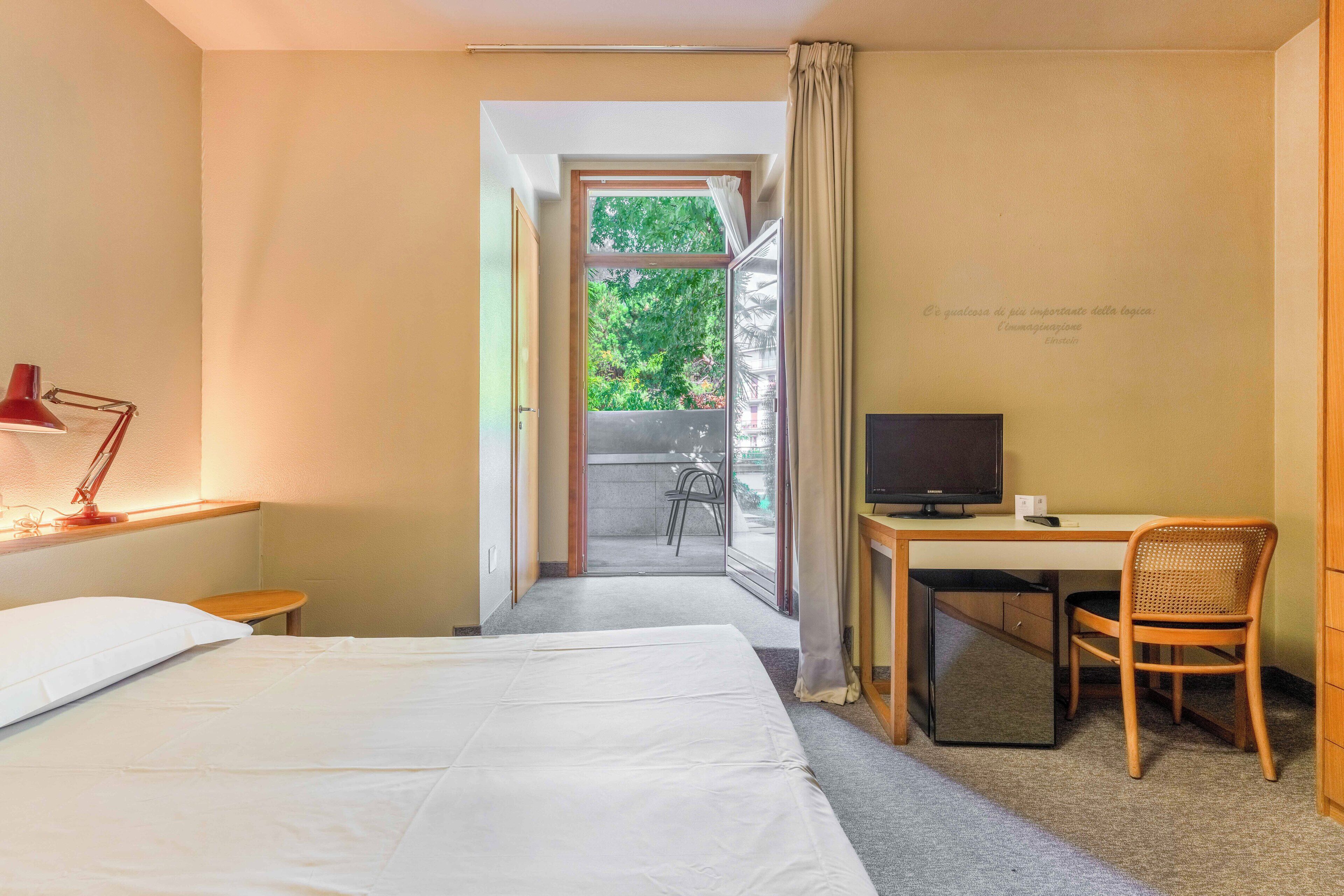 Une chambre d’hôtel équipée d’un lit, d’un bureau, d’une chaise, d’une télévision et offrant une vue sur l’extérieur.