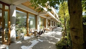 An outdoor cafe area with tables and chairs, large windows, and potted plants. - Albergo Sorriso (Darfo Boario Terme)