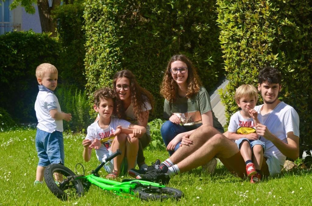 Een groep mensen zit op het gras met een groene fiets voor een haag.
