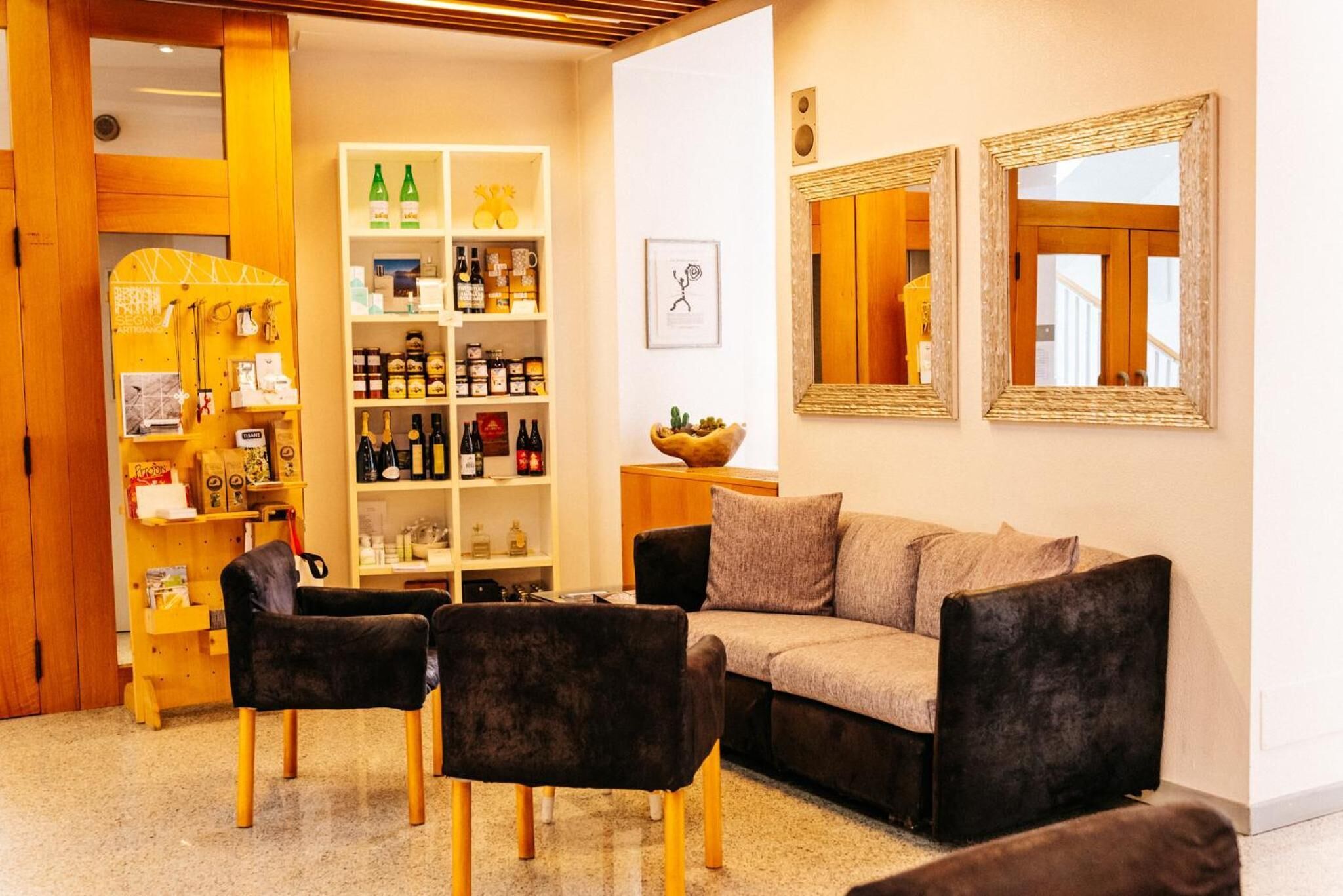 Una sala de estar acogedora con un sofá, dos sillones y una mesa de centro. Se observa una estantería llena de libros y objetos decorativos. En la pared hay un espejo y un cuadro enmarcado.