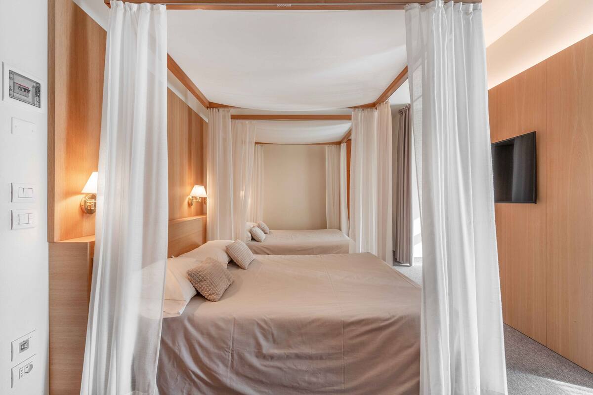 Een hotelkamer met twee bedden, een hemelbed, houten lambrisering, een flatscreen-tv en wandlampen.