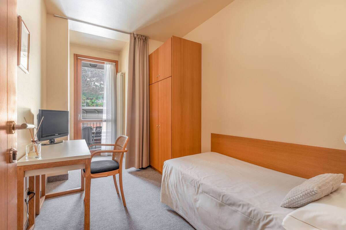 Een hotelkamer met een bed, een bureau met een computer, een stoel en een kledingkast.