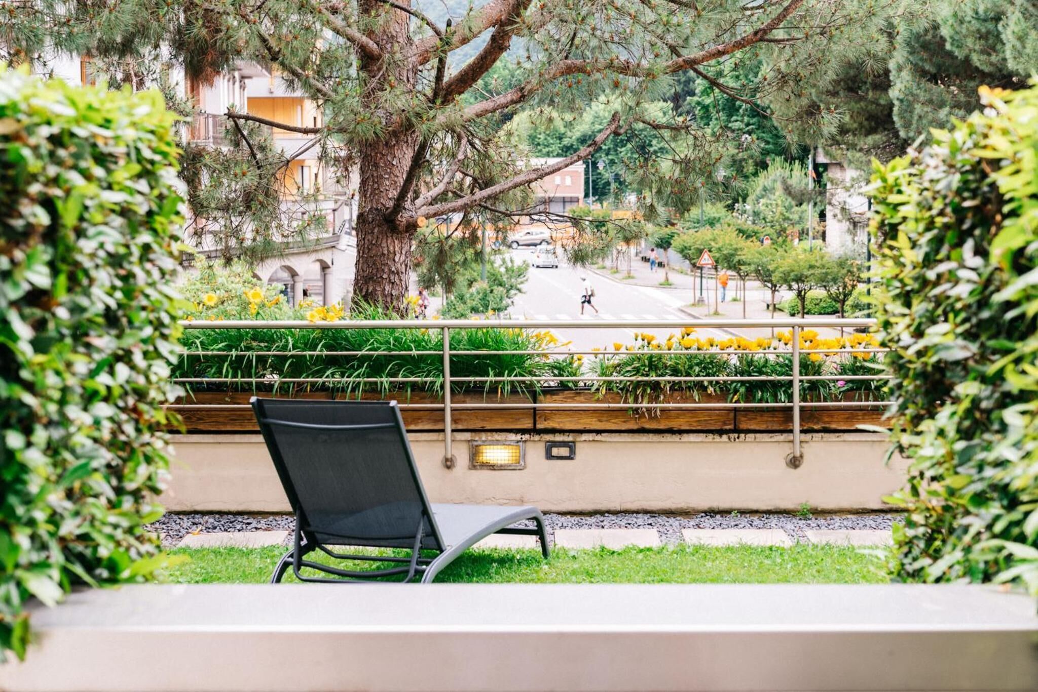 Un balcón con una silla, con vista a una calle llena de flores amarillas y árboles.
